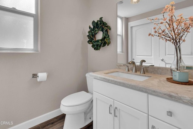 half bath featuring toilet, baseboards, plenty of natural light, and vanity