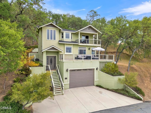 view of front facade featuring a garage, a balcony, concrete driveway, stairs, and stucco siding