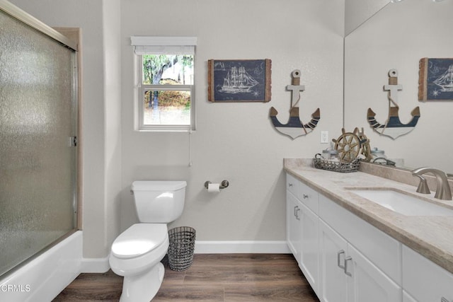 bathroom with vanity, wood finished floors, shower / bath combination with glass door, toilet, and baseboards