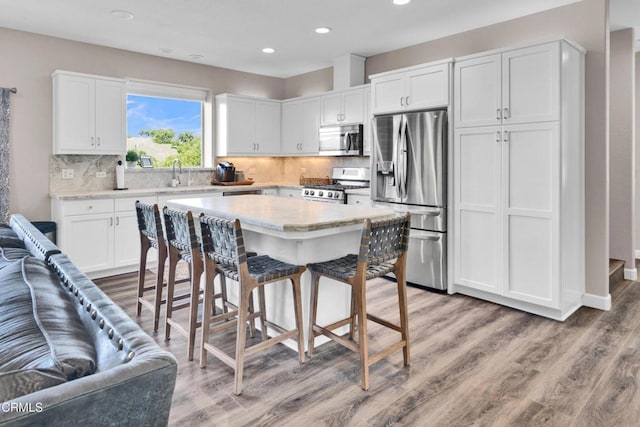 kitchen with white cabinetry, a breakfast bar, stainless steel appliances, recessed lighting, and light wood-style flooring
