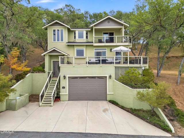 view of front facade with a balcony, stucco siding, stairs, an attached garage, and driveway