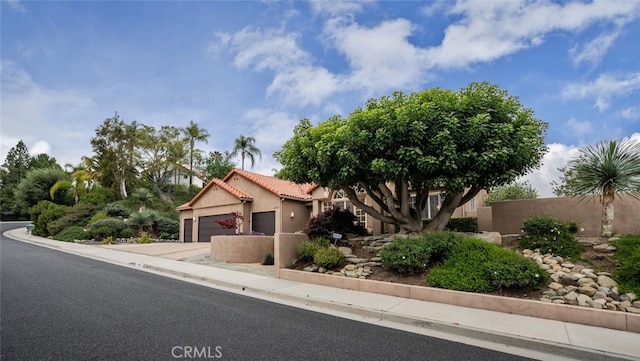 view of front facade featuring driveway, a tile roof, a garage, fence, and stucco siding