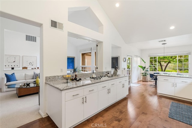 kitchen with visible vents, wood finished floors, white cabinets, and high vaulted ceiling