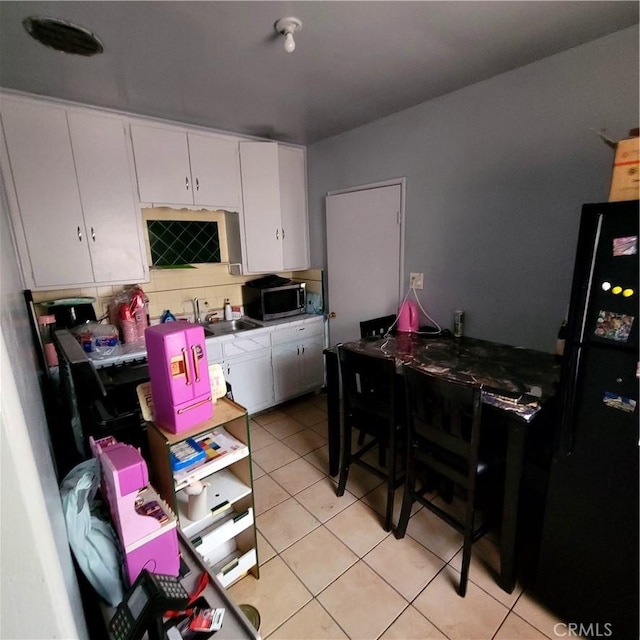 kitchen featuring light tile patterned flooring, a sink, freestanding refrigerator, white cabinetry, and stainless steel microwave