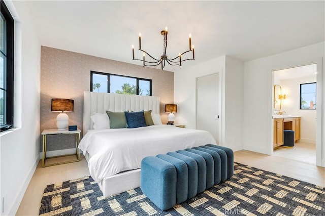 bedroom with connected bathroom, baseboards, a chandelier, and light wood finished floors