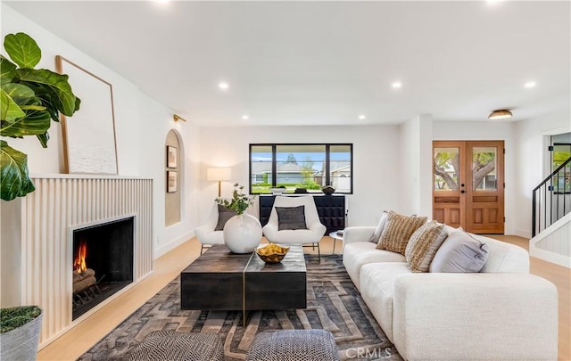 living room featuring wood finished floors, baseboards, a warm lit fireplace, stairway, and recessed lighting