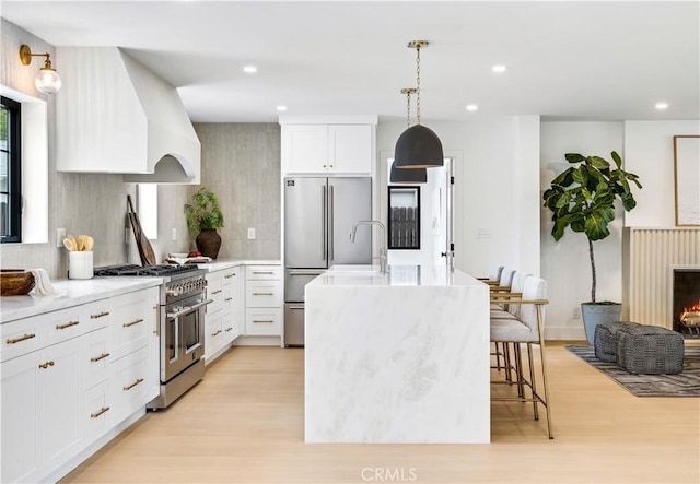 kitchen featuring a kitchen island with sink, high end appliances, light wood-type flooring, tasteful backsplash, and custom range hood