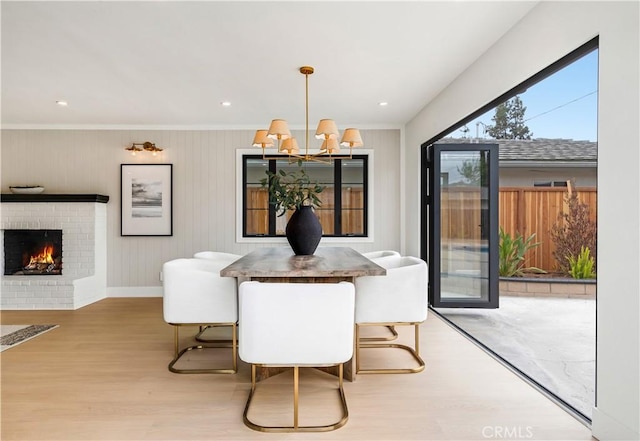 dining area featuring crown molding, a notable chandelier, a brick fireplace, baseboards, and wood finished floors