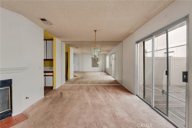 unfurnished dining area with a textured ceiling, visible vents, a fireplace with flush hearth, carpet floors, and an inviting chandelier