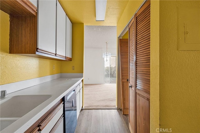 kitchen featuring electric panel, wood finished floors, dishwasher, a sink, and a textured wall