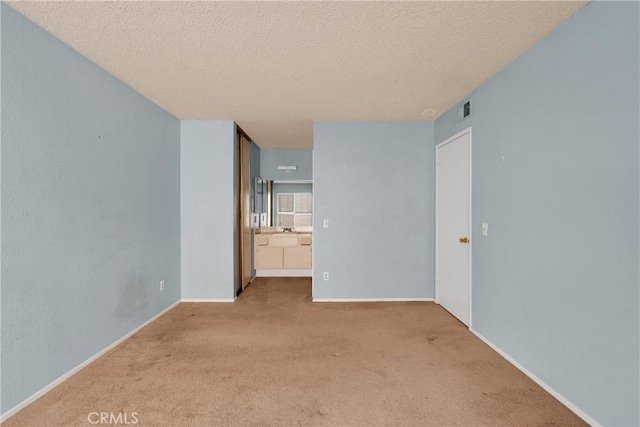 unfurnished room with a textured ceiling, visible vents, light carpet, and baseboards