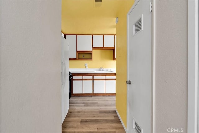 hall with visible vents, a sink, and light wood-style flooring