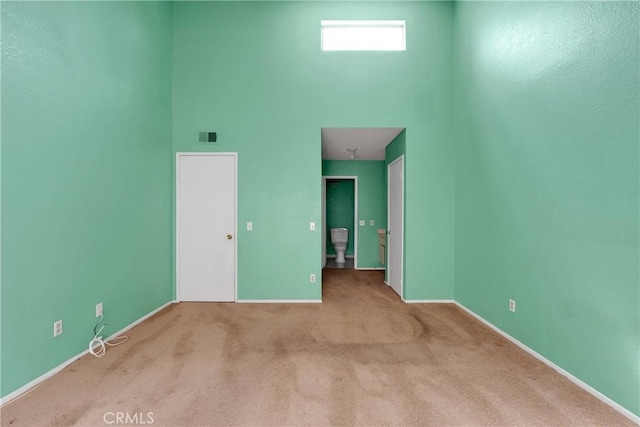 spare room with carpet floors, a high ceiling, baseboards, and visible vents