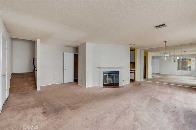 unfurnished living room featuring visible vents, stairs, a textured ceiling, a fireplace with flush hearth, and carpet