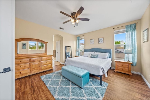 bedroom with arched walkways, baseboards, wood finished floors, and visible vents