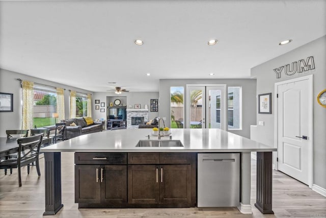 kitchen featuring dark brown cabinetry, stainless steel dishwasher, a sink, light countertops, and light wood-style floors