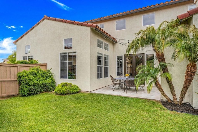 rear view of house with fence, stucco siding, a patio area, a lawn, and a tiled roof
