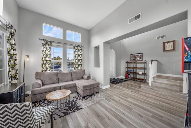 living room featuring visible vents, baseboards, a high ceiling, arched walkways, and light wood finished floors