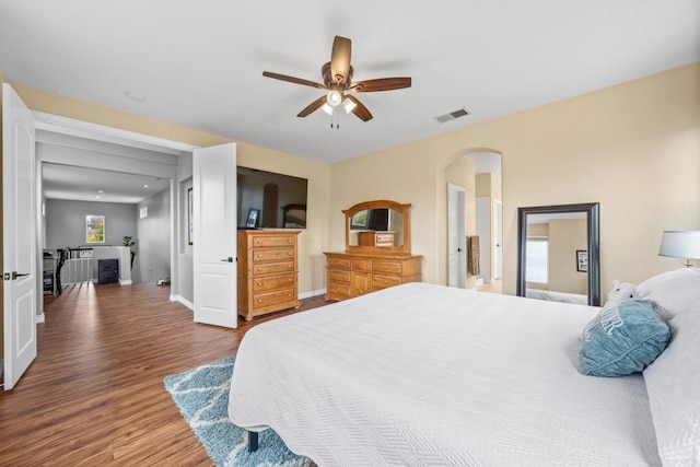 bedroom with ceiling fan, arched walkways, baseboards, wood finished floors, and visible vents