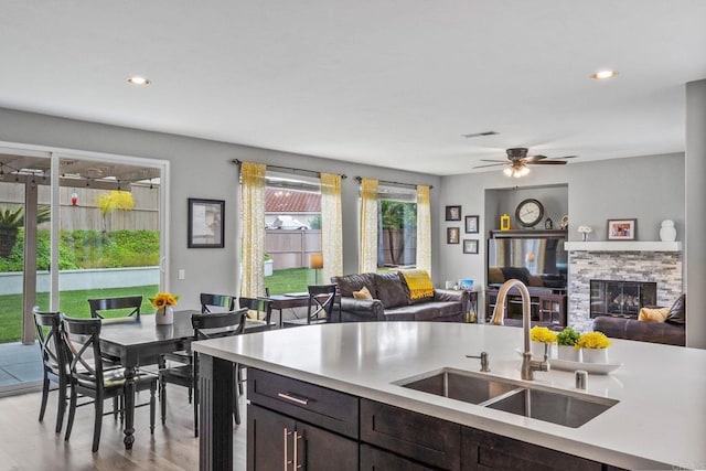 kitchen featuring a sink, light countertops, a stone fireplace, and dark brown cabinets