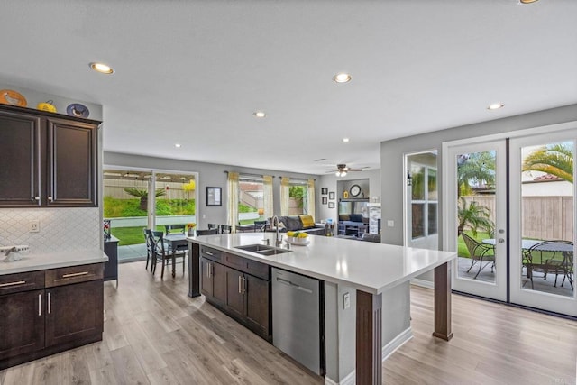 kitchen featuring stainless steel dishwasher, dark brown cabinets, a sink, light countertops, and light wood finished floors