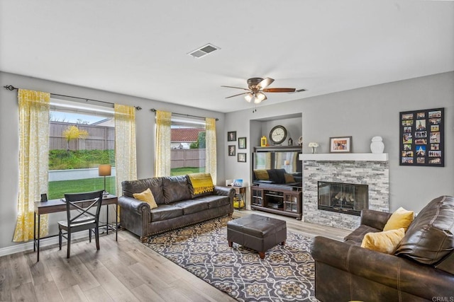 living room with visible vents, ceiling fan, wood finished floors, and a stone fireplace
