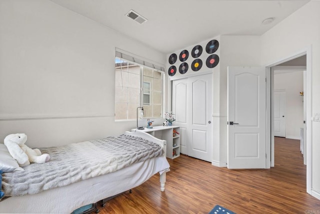bedroom with baseboards, a closet, wood finished floors, and visible vents