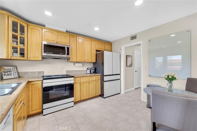 kitchen featuring visible vents, white appliances, glass insert cabinets, baseboards, and a sink