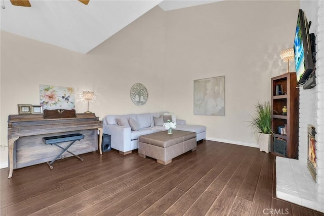 living room featuring ceiling fan, a brick fireplace, wood finished floors, high vaulted ceiling, and baseboards