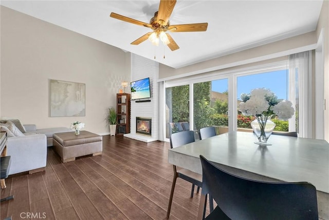 dining area featuring a fireplace, a ceiling fan, baseboards, vaulted ceiling, and dark wood-style floors