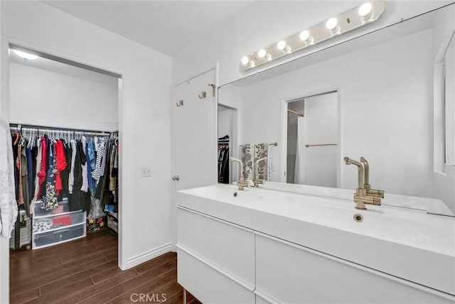 bathroom featuring double vanity, a shower, wood finished floors, baseboards, and a spacious closet