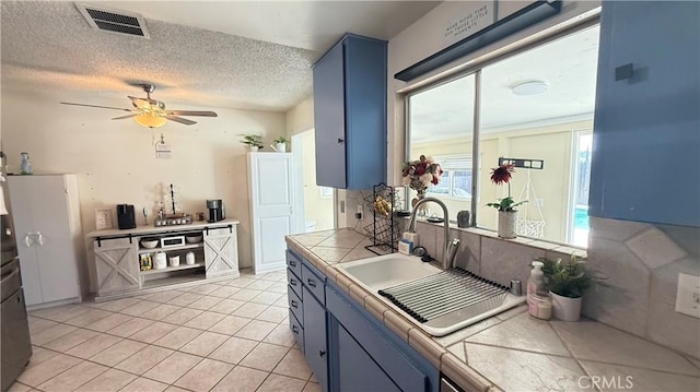 kitchen featuring tile counters, blue cabinetry, visible vents, and a sink