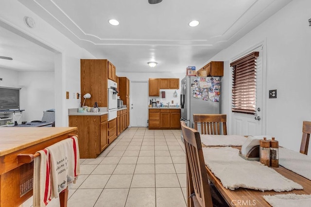 kitchen with freestanding refrigerator, light tile patterned flooring, brown cabinets, and white oven