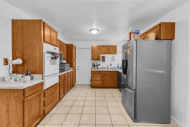 kitchen with brown cabinetry, appliances with stainless steel finishes, a sink, light tile patterned floors, and a warming drawer