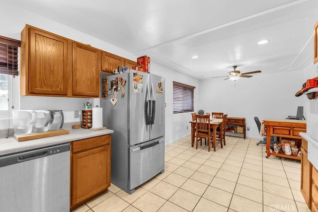kitchen with light countertops, brown cabinetry, stainless steel appliances, a ceiling fan, and light tile patterned floors