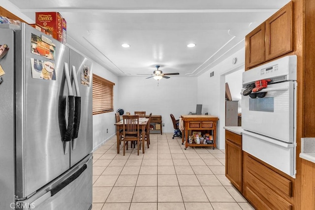 kitchen with brown cabinetry, white oven, light tile patterned floors, freestanding refrigerator, and a warming drawer