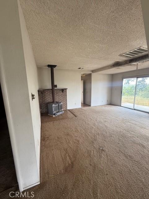 unfurnished living room featuring carpet flooring, a textured ceiling, visible vents, and a wood stove