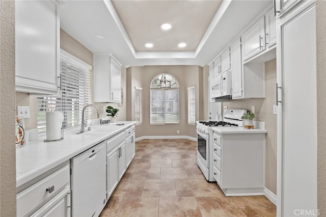 kitchen featuring baseboards, a sink, white appliances, and light countertops