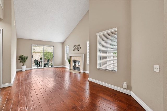 unfurnished living room featuring baseboards, dark wood-style floors, high vaulted ceiling, and a tile fireplace