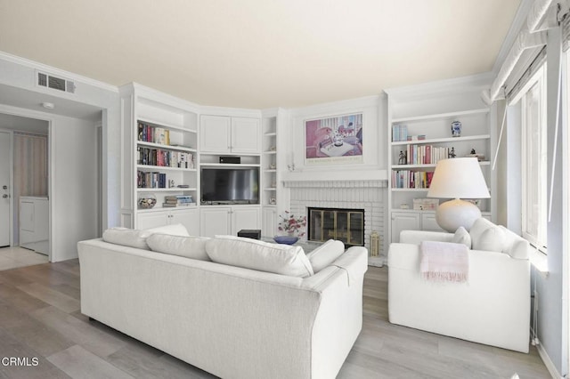 living room with visible vents, ornamental molding, light wood-style floors, and a brick fireplace