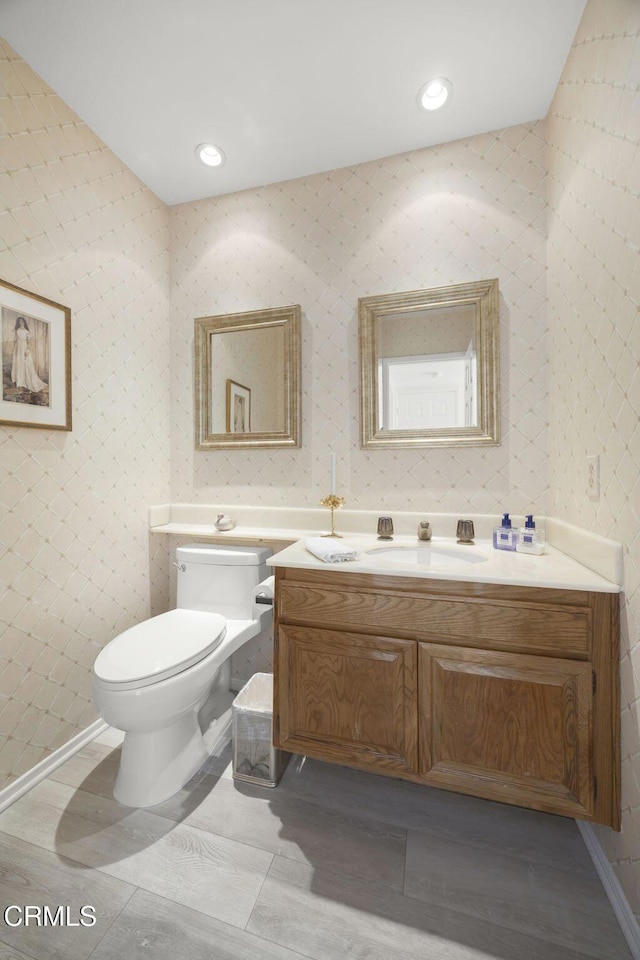 half bathroom with vanity, recessed lighting, and toilet