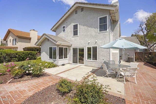 rear view of house with fence, a gate, stucco siding, and a patio area