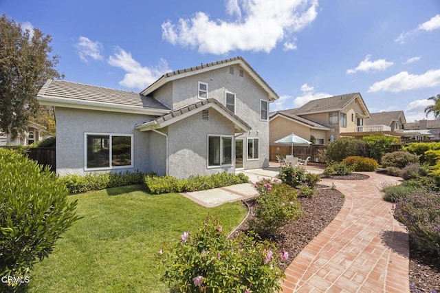 rear view of house with a tile roof, a lawn, fence, a patio, and stucco siding