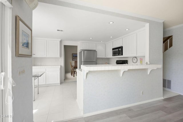 kitchen featuring visible vents, freestanding refrigerator, a peninsula, a kitchen bar, and white cabinets