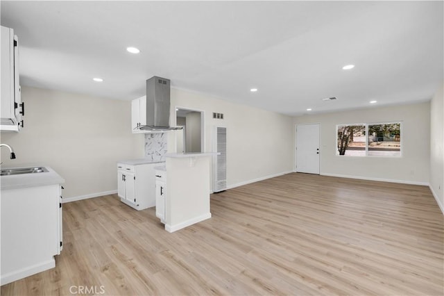kitchen with light countertops, a sink, island exhaust hood, and light wood-style flooring