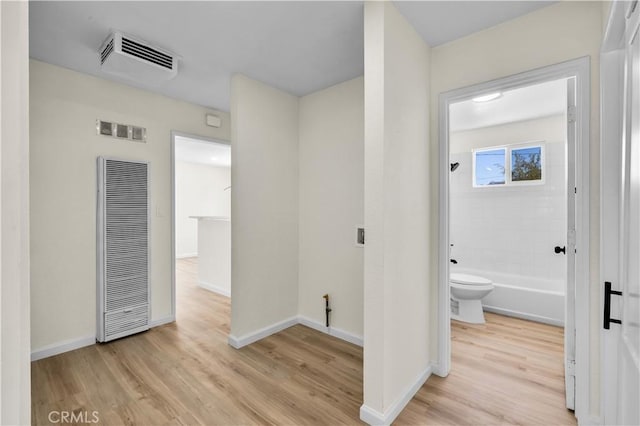 hall featuring a heating unit, visible vents, baseboards, and light wood finished floors