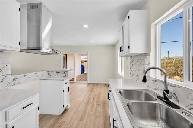 kitchen with a sink, backsplash, white cabinetry, and island range hood