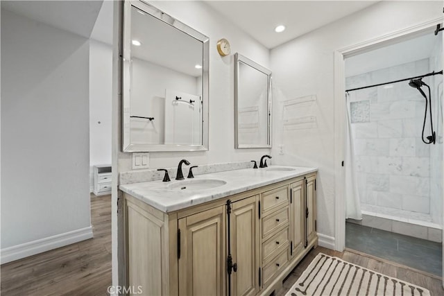 bathroom featuring baseboards, a tile shower, a sink, and wood finished floors