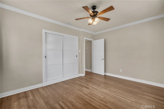 unfurnished bedroom featuring baseboards, wood finished floors, visible vents, ornamental molding, and a closet