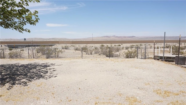 view of yard featuring a mountain view, view of desert, and fence